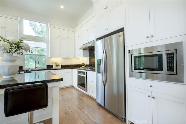 kitchen with appliances with stainless steel finishes, light hardwood / wood-style floors, dark stone counters, and white cabinets