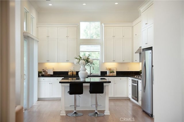 kitchen with white cabinetry, stainless steel appliances, a center island, sink, and a kitchen bar