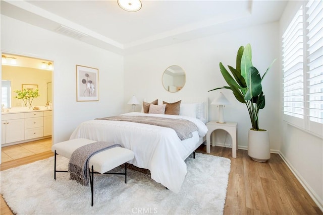 bedroom with a raised ceiling, light wood-type flooring, and ensuite bath