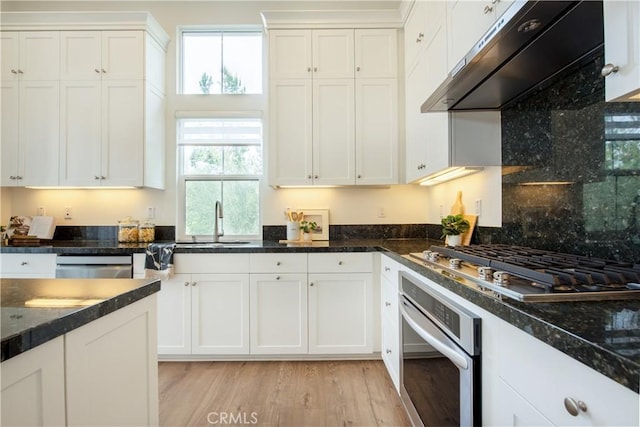 kitchen featuring dark stone counters, appliances with stainless steel finishes, white cabinets, and range hood