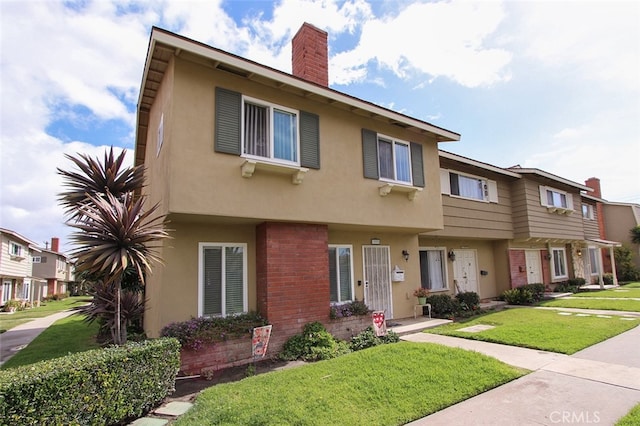 townhome / multi-family property featuring brick siding, a chimney, a front lawn, and stucco siding