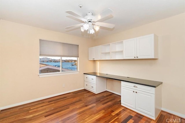 unfurnished office featuring dark wood-type flooring, built in desk, and ceiling fan