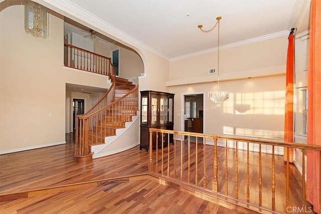 hall featuring hardwood / wood-style floors, crown molding, a chandelier, and a towering ceiling