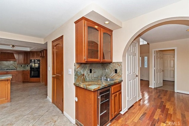 kitchen featuring sink, wine cooler, light stone counters, black appliances, and custom range hood