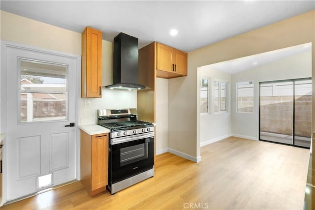 kitchen featuring wall chimney range hood, stainless steel gas range oven, lofted ceiling, and light hardwood / wood-style floors