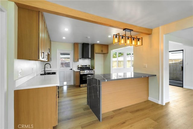 kitchen with light hardwood / wood-style flooring, stainless steel gas range oven, wall chimney range hood, pendant lighting, and sink