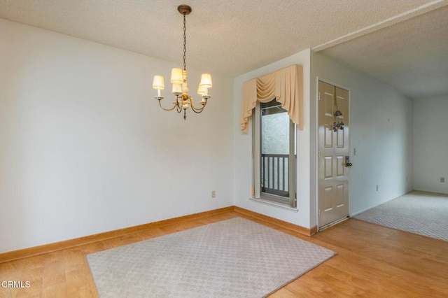 spare room featuring an inviting chandelier, wood-type flooring, and a textured ceiling