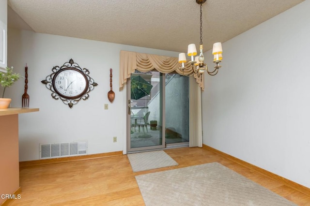 unfurnished dining area featuring an inviting chandelier, wood-type flooring, and a textured ceiling