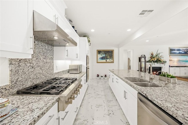 kitchen with sink, light stone counters, appliances with stainless steel finishes, range hood, and white cabinets