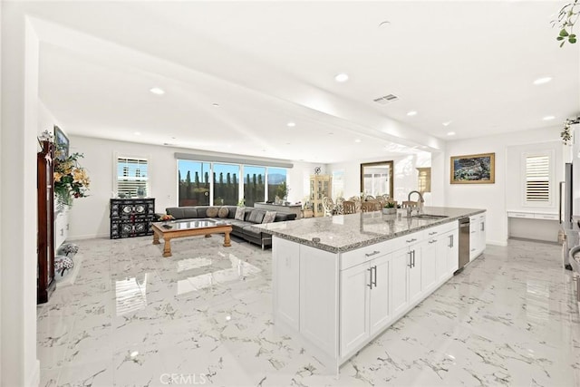 kitchen featuring sink, white cabinets, a kitchen island with sink, stainless steel dishwasher, and light stone countertops