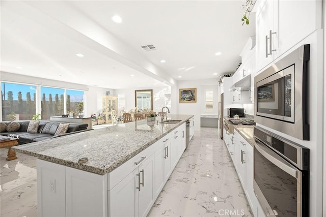 kitchen featuring a spacious island, sink, white cabinetry, light stone counters, and stainless steel appliances