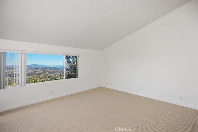 spare room featuring carpet flooring, vaulted ceiling, baseboards, and a mountain view