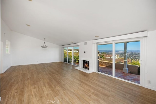 unfurnished living room with wood finished floors, visible vents, baseboards, vaulted ceiling, and a brick fireplace