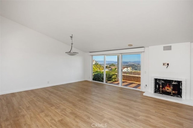 unfurnished living room featuring vaulted ceiling, a fireplace, light wood-style flooring, and baseboards