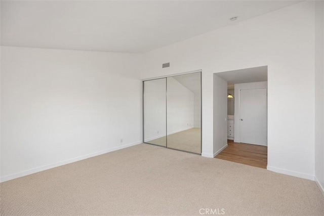 unfurnished bedroom featuring visible vents, baseboards, a closet, and light colored carpet