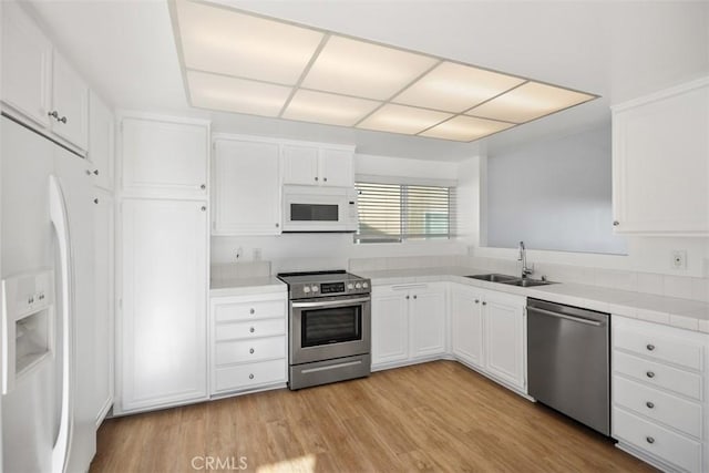 kitchen featuring light wood-style flooring, a sink, white cabinetry, light countertops, and appliances with stainless steel finishes