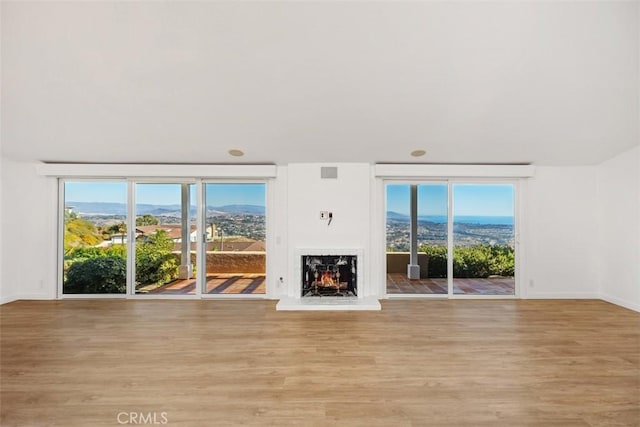 unfurnished living room with a warm lit fireplace, light wood finished floors, and a healthy amount of sunlight