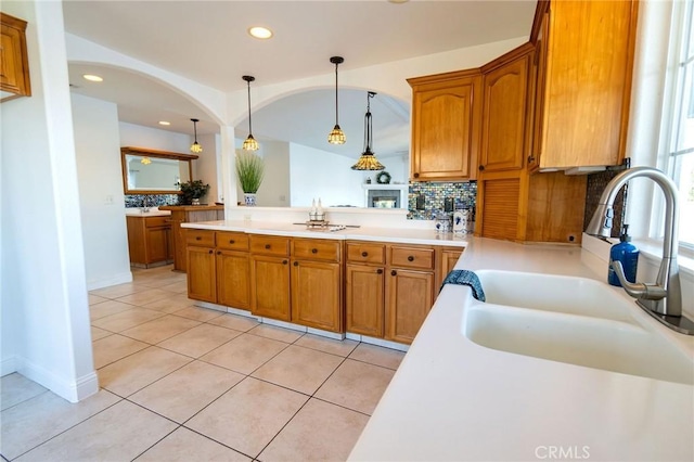 kitchen featuring sink, decorative light fixtures, light tile patterned floors, kitchen peninsula, and backsplash