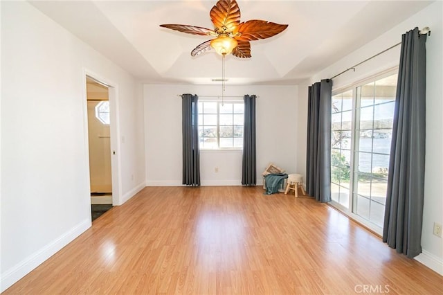 unfurnished room with light hardwood / wood-style flooring, a raised ceiling, ceiling fan, and plenty of natural light