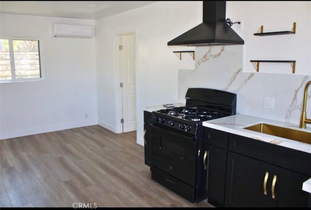 kitchen featuring wall chimney exhaust hood, sink, black gas range oven, a wall unit AC, and light hardwood / wood-style floors