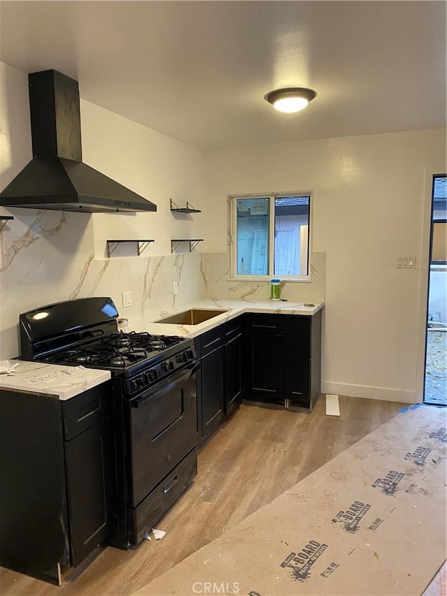 kitchen with tasteful backsplash, ventilation hood, light hardwood / wood-style flooring, and black gas range oven