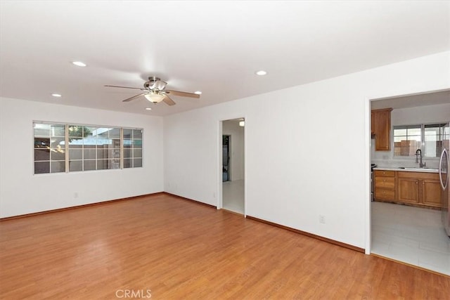 empty room featuring light wood finished floors, baseboards, a ceiling fan, a sink, and recessed lighting