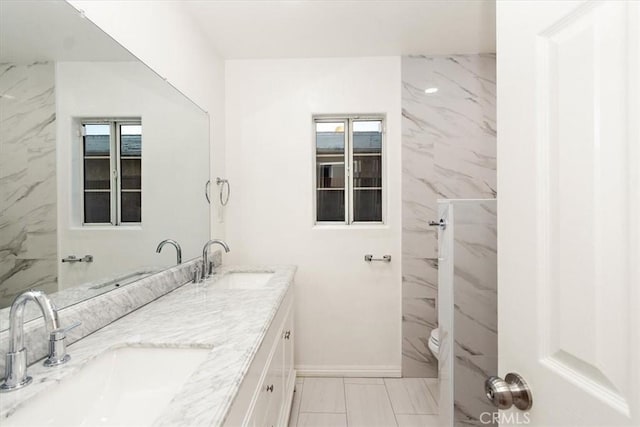 full bathroom featuring double vanity, baseboards, toilet, and a sink