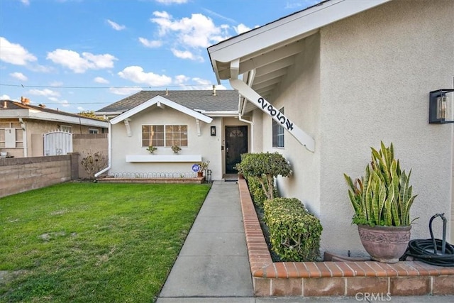 property entrance with roof with shingles, fence, a lawn, and stucco siding