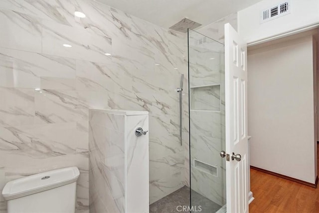 bathroom with toilet, a marble finish shower, visible vents, and wood finished floors