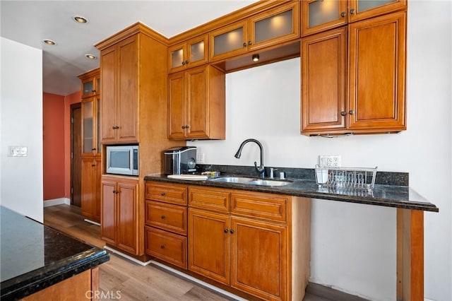 kitchen featuring stainless steel microwave, dark stone counters, sink, and light wood-type flooring