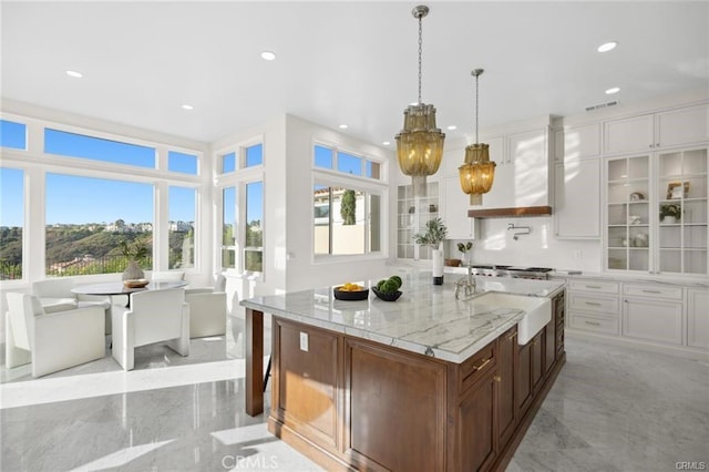 kitchen with pendant lighting, white cabinetry, sink, custom range hood, and a center island with sink