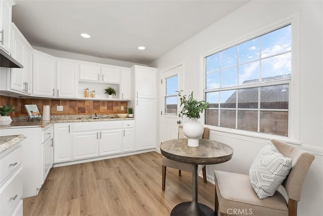 kitchen featuring sink, light hardwood / wood-style flooring, backsplash, light stone counters, and white cabinets