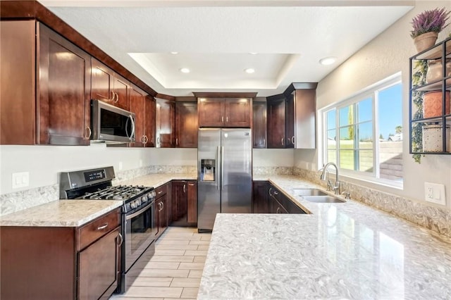 kitchen with sink, light stone countertops, a raised ceiling, and appliances with stainless steel finishes