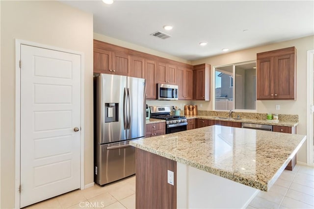 kitchen featuring visible vents, a sink, light stone counters, a kitchen island, and appliances with stainless steel finishes