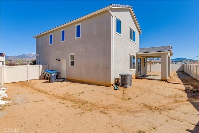 back of property with a fenced backyard, a mountain view, central AC, and stucco siding