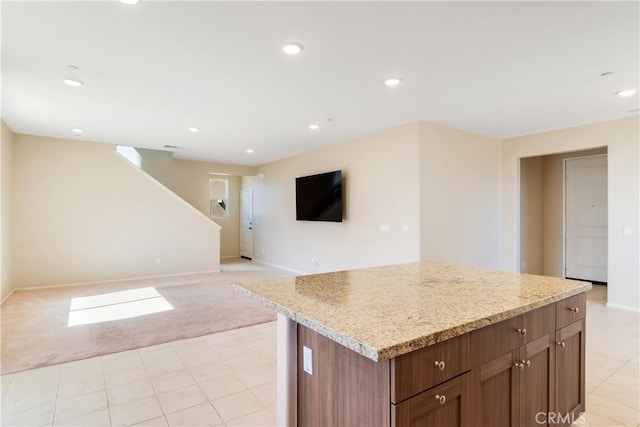 kitchen with light stone counters, a kitchen island, recessed lighting, light carpet, and open floor plan