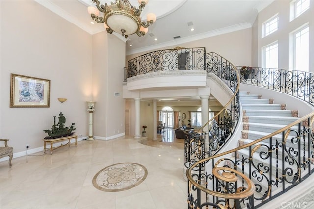 foyer with crown molding, decorative columns, a chandelier, and a towering ceiling