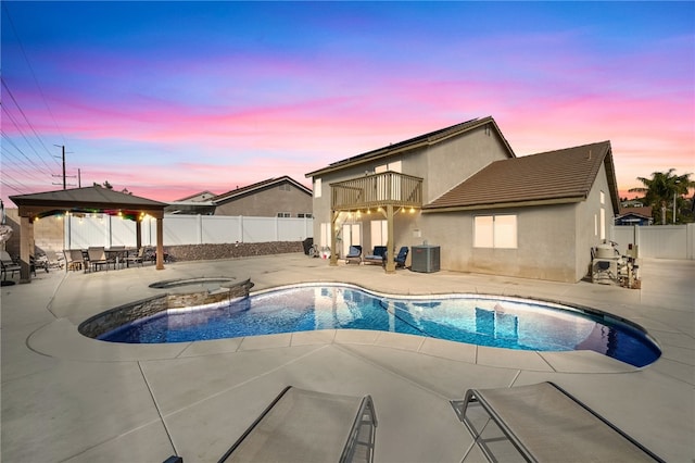 pool at dusk featuring cooling unit, a patio area, an in ground hot tub, and a gazebo