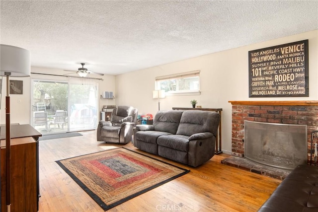 living room featuring plenty of natural light, hardwood / wood-style floors, a textured ceiling, and a brick fireplace