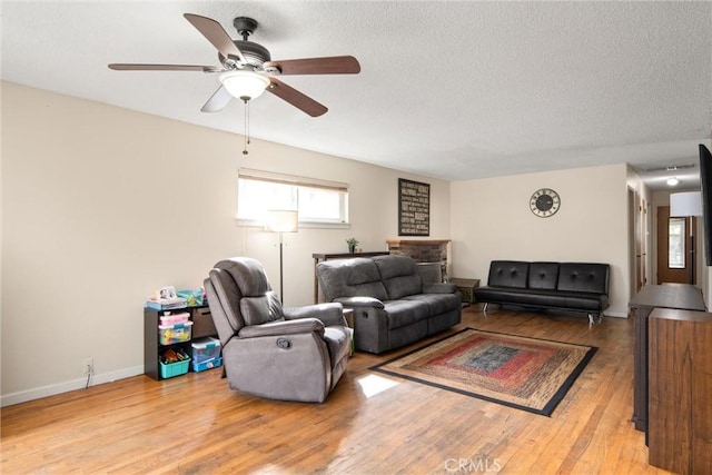 living room featuring ceiling fan, light hardwood / wood-style flooring, and a textured ceiling