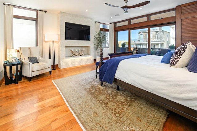 bedroom featuring a multi sided fireplace, wood-type flooring, access to outside, and ceiling fan