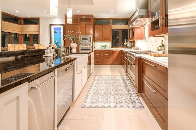 kitchen with appliances with stainless steel finishes, dark stone counters, decorative light fixtures, ventilation hood, and backsplash