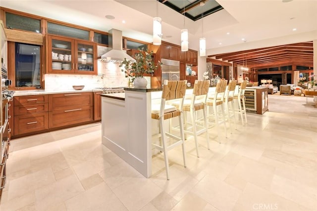 kitchen featuring hanging light fixtures, range hood, a center island, built in fridge, and a kitchen bar