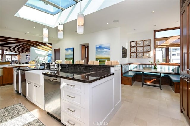 kitchen with white cabinets, dark stone countertops, a center island with sink, and stainless steel dishwasher