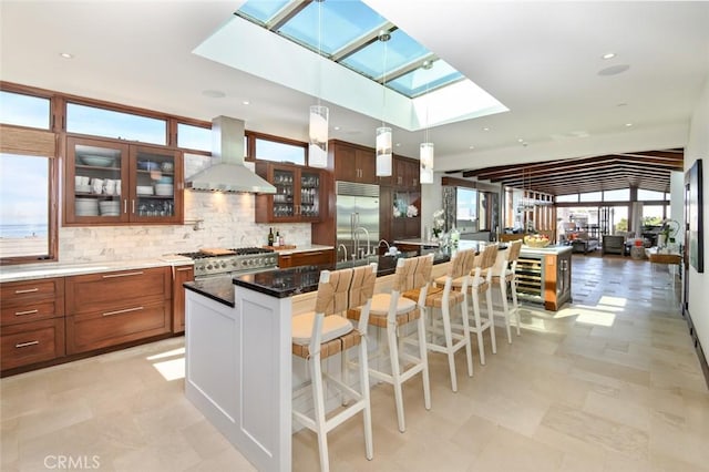 kitchen with a breakfast bar area, range hood, premium appliances, pendant lighting, and a center island