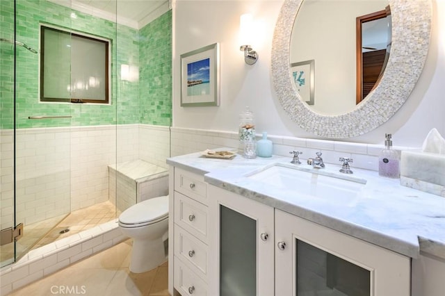 bathroom featuring tile patterned floors, toilet, tile walls, vanity, and tiled shower