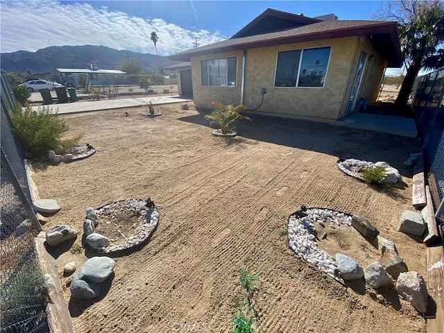 rear view of house featuring stucco siding, a mountain view, a patio, and fence