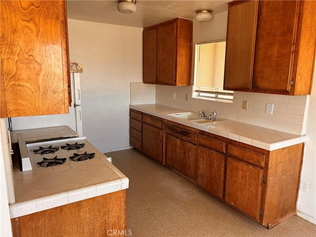 kitchen featuring a sink, light countertops, backsplash, brown cabinets, and light floors