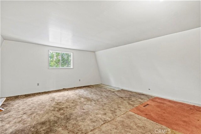 carpeted empty room with vaulted ceiling