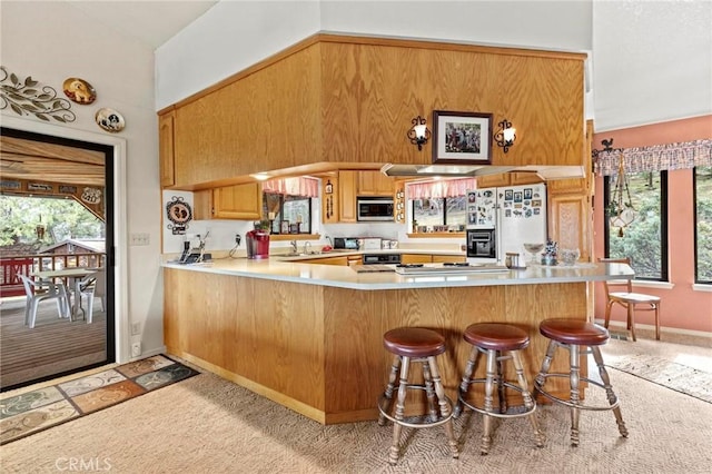 kitchen featuring sink, a breakfast bar area, white refrigerator with ice dispenser, kitchen peninsula, and light carpet